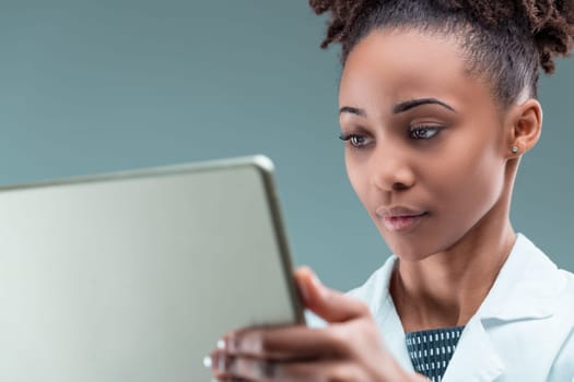 Dedicated young woman in a lab coat immerses herself in research on her handheld device