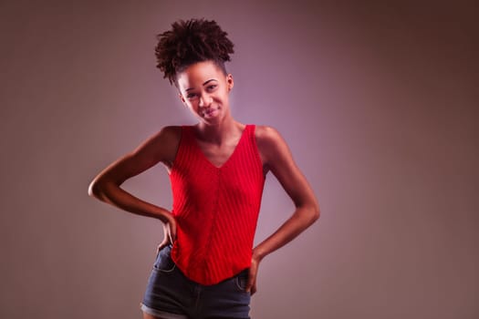 Young woman in a red knit top and denim shorts strikes a playful pose with a wink