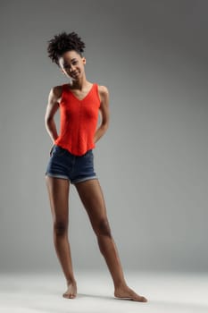 Young beautiful black woman in red tank top and denim shorts stands confidently