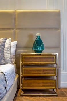 A bedroom with hardwood flooring, featuring a wooden bed and a nightstand made of cabinetry. The nightstand has a vase on top, adding a natural touch to the room