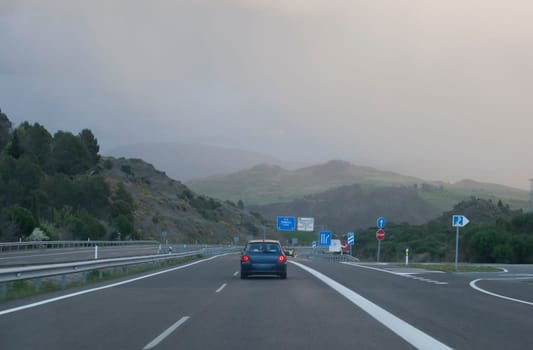 Wind turbines on the top of the hills. Vehicle approaching some foggy mountains