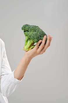 Healthy eating concept. Hand holds broccoli over grey background.