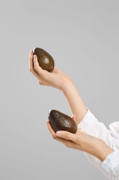 Female hands hold two whole avocado