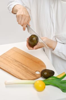 Unrecognizable woman cutting fresh avocado into halves. Concept of balanced eating.