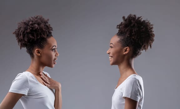 Young black woman whispers gossip, eliciting a knowing smile from her reflection, suggesting self-talk