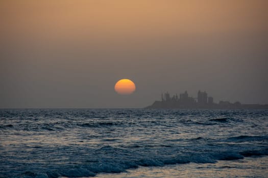 Sunset over the sea with a city in silhouette in the background