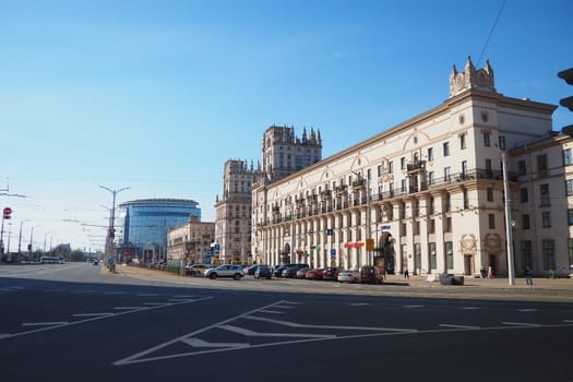 Minsk, Belarus, April 10, 2024: Station Square in front of the railway station. Cars, trucks and buses pass by. People are walking. Sunny spring day. Majestic tower buildings and Kirov Avenue.