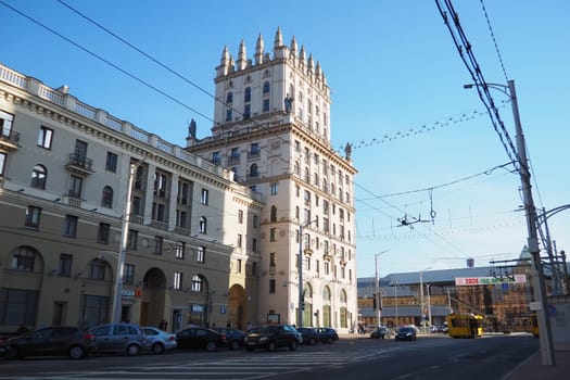 Minsk, Belarus, April 10, 2024: Station Square in front of the railway station. Cars, trucks and buses pass by. People are walking. Sunny spring day. Majestic tower buildings and Kirov Avenue.