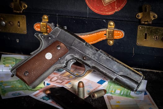 a close up of colt 1911, ammos and money, suitcase on background
