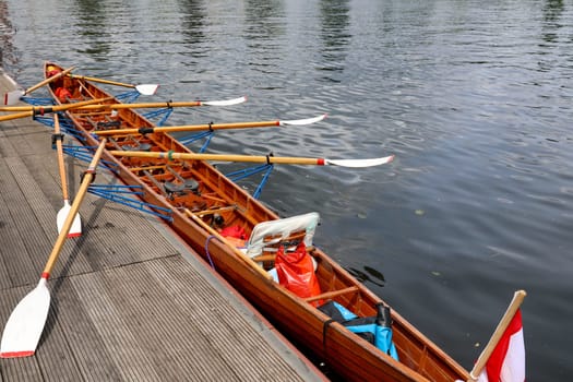 A rowing boat, multi-seater has moored to a jetty at a boathouse.