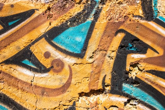 Detail of ocher and turquoise colors graffiti painted on the wall of a ruin, photogaphed in Portugal
