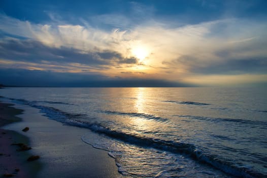 Sunset, illuminated sea. Sandy beach in the foreground. Light waves. Baltic Sea. Landscape on the coast