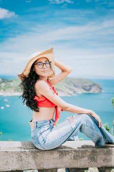 Beautiful tourist girl in a viewpoint with a beach in the background. Happy tourist sitting at a viewpoint looking at the camera with bay in the background