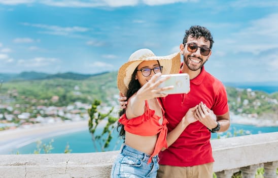 Happy Young tourist couple taking a selfie in a beautiful viewpoint. Smiling tourist couple taking a selfie at the viewpoint of San Juan del Sur.