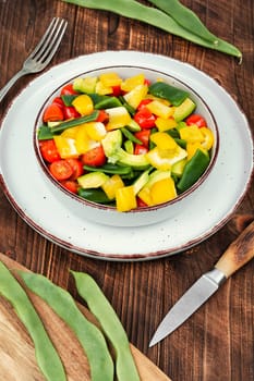 Vegetable salad with bell pepper, tomato, avocado and runner beans in bowl on rustic wooden table. Rustic style.