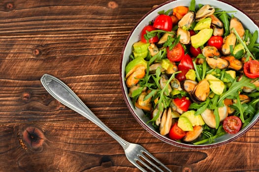 Homemade tasty salad of mussels, arugula, tomato and avocado on rustic wooden table. Space for text.