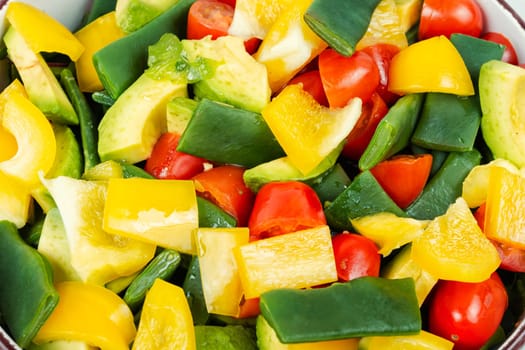 Vegetable salad with bell pepper, tomato, avocado and runner beans in bowl on rustic wooden table. Rustic style.
