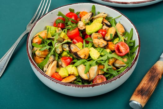 Homemade tasty salad of mussels, arugula, tomato and avocado on rustic wooden table. Space for text.