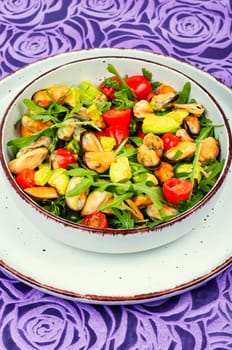 Homemade tasty salad of mussels, arugula, tomato and avocado on rustic wooden table. Space for text.