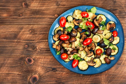 Mushrooms, zucchini and tomatoes baked in the oven on rustic wooden table. Copy space.