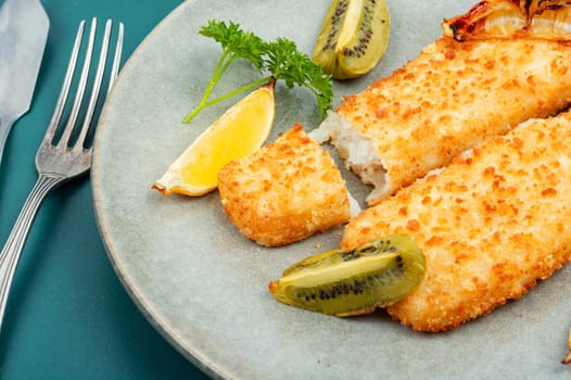 Pollock fillet roasted in bread crumbs served with sauce and kiwi. Fish in chips.