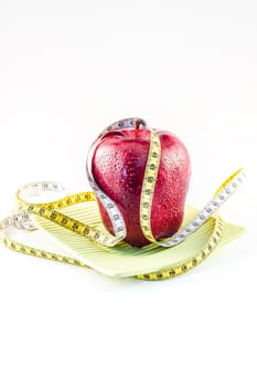 Red apple and tape measure on a plate on a white background. Selective focus with shallow depth of field.