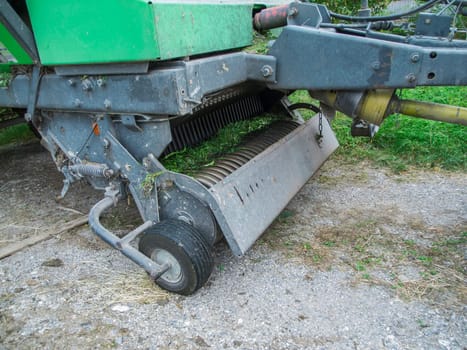 Partial view of the PTO spring tines and pickup roller of a baler on a gravel surface after intensive use.