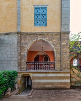 A serene view of a rustic style building featuring an arched wooden balcony, and detailed window grills
