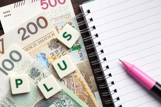 Polish social program called 800 plus. Background concept with polish money, word plus and notebook with pen on wooden table. Copy space. Top view