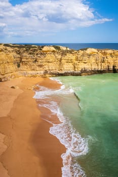 Vertical view of cliffs and ocean waves crashing onto Praia da Ponta Pequena beach near Albufeira, Algarve, Portugal