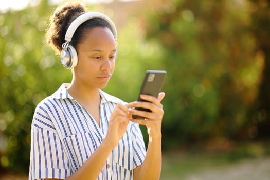 Black woman wearing headphone using phone waling in a garden