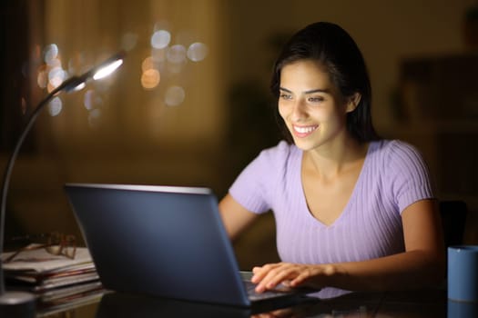 Happy woman sitting at home using a laptop in the night