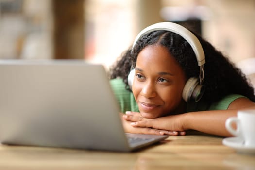 Satisfied black woman with headphone watching media content on laptop in a restaurant terrace