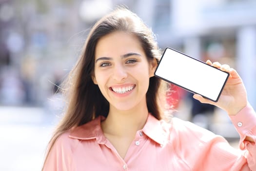 Front view portrait of an elegant happy woman showing blank phone screen in the street