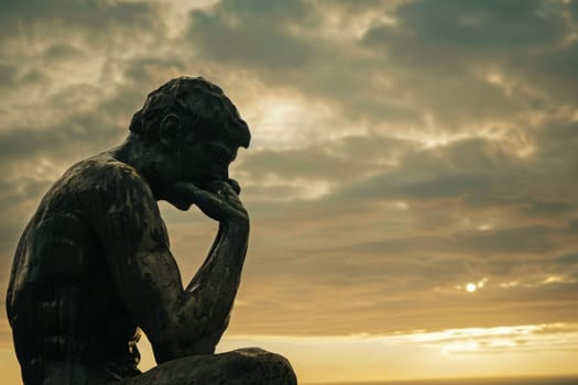 A thoughtful statue silhouetted by a warm-hued sky as the day fades.
