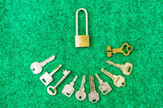 Brass Padlock and many types of keys on green carpet background.
