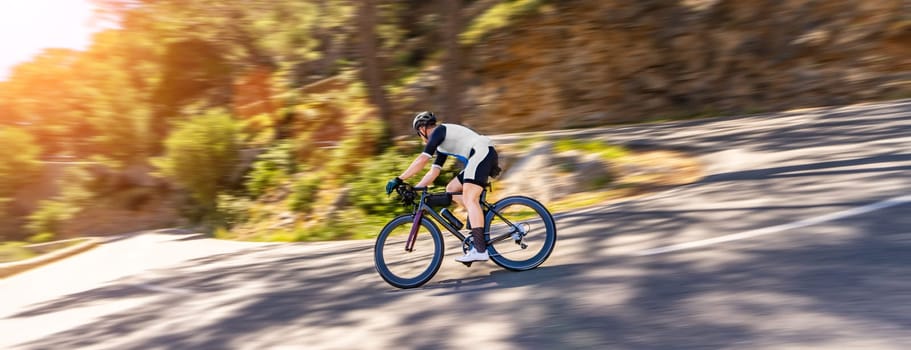 Mature Adult on a racing bike climbing the hill at mediterranean sea landscape coastal mountain road - mallorca mountains