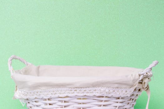 Empty wicker basket over light green glittering background. For your food and product display assembly. Macro of a straw basket.