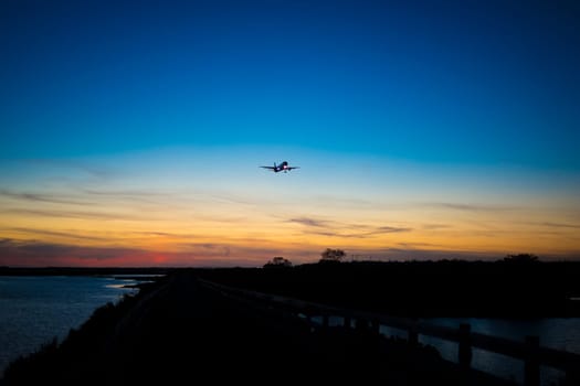 Airplane in silhouette approaching the airport of Faro, over Ria Formosa natural park during sunset
