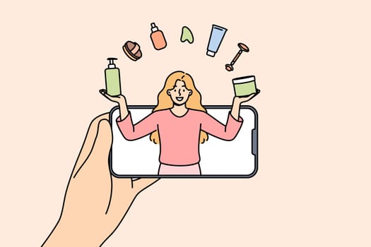 Woman beauty blogger juggles with cosmetics, looking out from mobile phone screen, giving tips on applying makeup. Girl beauty blogger tells lifehacks for facial skin care or getting rid of wrinkles