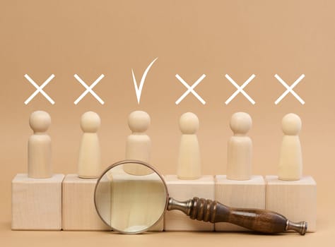 Wooden figures of men stand on a beige background and a wooden magnifying glass. Recruitment concept, search for talented and capable employees, career growth