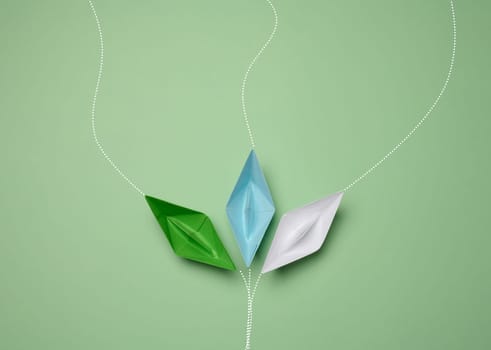 Paper boats on a green background with paths of movement, representing the concept of individuality. Top view
