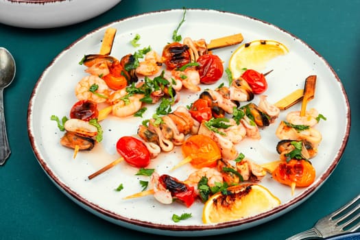 Grilled squid, fried mussels and shrimps, prawns fried on sticks on white plate.