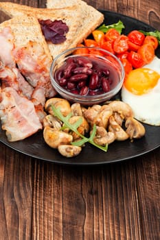 Fried bacon and eggs, toast and beans and vegetables. Traditional English breakfast.