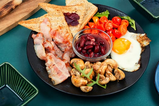 Fried bacon and eggs, toast and beans and vegetables. Traditional English breakfast.