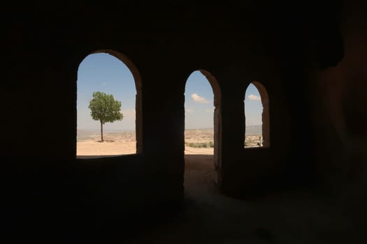 View out of some windows of the Uchisar Castle, Kalesi onto a tree and the landscape of Cappadocia, Turkey 2022