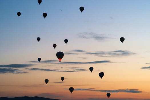 Hot air balloons rising over the landscape of the Red Valley, Rose Valley before sunrise, close to Goreme, Cavusin, Cappadocia, Turkey 2022