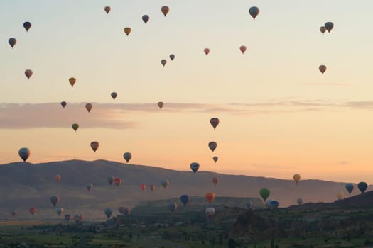 Dozens of colorful hot air balloons over the landscape of the Red Valley, Rose Valley right before sunrise, close to Goreme, Cavusin, Cappadocia, Turkey 2022