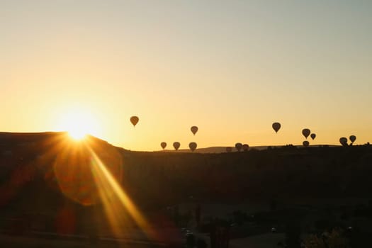 Hot air balloons coming over the edge of a hill where the sun is about to rise, Göreme view point, Cappadocia, Turkey 2022