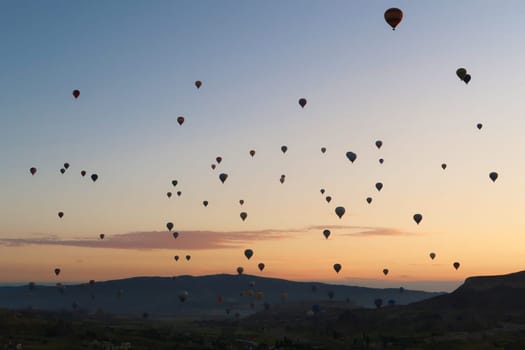 Dozens of hot air balloons rising over the landscape of the Red Valley, Rose Valley before sunrise, close to Goreme, Cavusin, Cappadocia, Turkey 2022